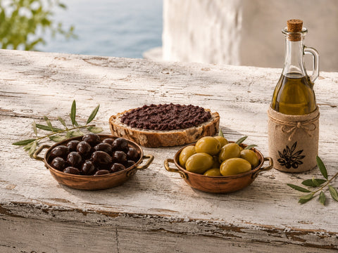Griechisches Olivenöl extra mit grünen und schwarzen Oliven sowie Olivenpaste auf Brot